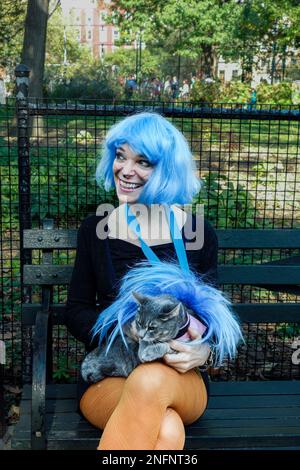 Eine Frau in blauer Perücke hält ein Haustier mit blauem Federkostüm in der Tompkins Park Halloween Dog Parade, East Village, New York City, NY, USA Stockfoto