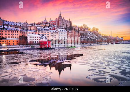 Stockholm, Schweden. Mariaberget und Sodermalm im Winter. Wunderschöner Himmel in Orange, Violett und Rosa bei Sonnenuntergang, reflektiert im gefrorenen Wasser des Mala-Sees Stockfoto