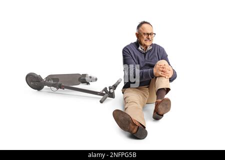 Reifer Mann mit einem elektrischen Roller, der sein schmerzhaftes Knie hält und isoliert auf weißem Hintergrund auf dem Boden sitzt Stockfoto
