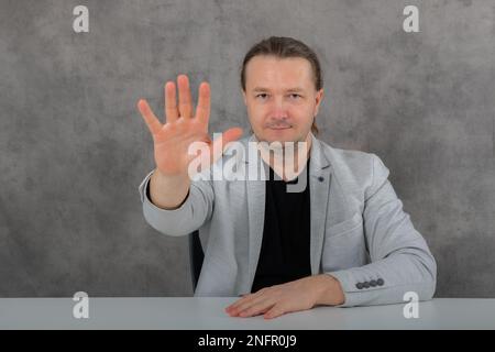 Ein Mann in einem grauen Anzug zeigt ein Stoppschild Stockfoto