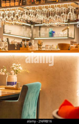 Restaurantinnenraum, verschwommen. Leere Theke mit hängenden Gläsern. Café-Design. Blumen auf dem Tisch im Café. Restaurantgeschäft. Café drinnen. Stockfoto