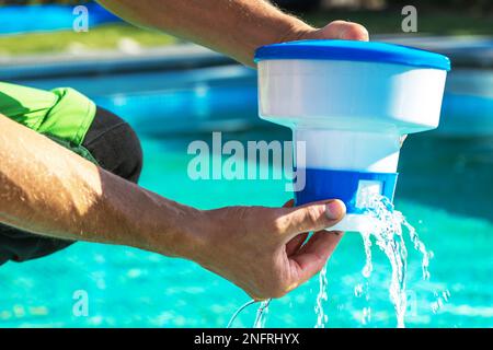Nahaufnahme des schwimmenden Chemikalienspenders in den Händen eines professionellen Schwimmbadtechnikers während der planmäßigen Wartung. Stockfoto
