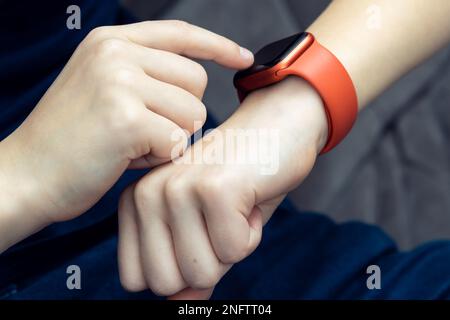 Unerkannter Teenager, männliche Hand, die auf der roten Smartwatch am Handgelenk tippt, Zeittechnologie. Puls-Herz-Check, Fitness-Tracker und Gesundheit des Kardiogramms Stockfoto