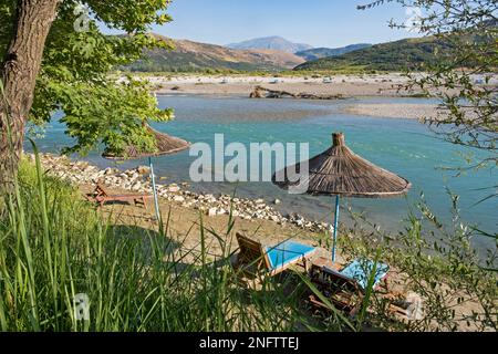 Sonnenschirme und leere Liegesitze am Ufer des Flusses Vjosë/Vjosa im Sommer, Lumi Vjosë, Lumi Drino im Südwesten Albaniens Stockfoto