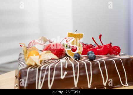 Schokoladen-Geburtstagskuchen mit Beeren und goldenen Kerzen Nummer 3 auf weißem Hintergrund, Kopie space.greetings,A Nummer Kerze leuchtet zur Feier Stockfoto