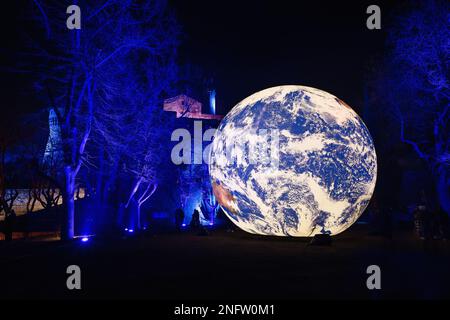 Brescia - Italia. 15. Februar 2023: Light is Life (Festa delle Luci A2A), „Floating Earth“ von Luke Jerram inmitten von blau beleuchteten Winterbäumen mit Torre dei Stockfoto
