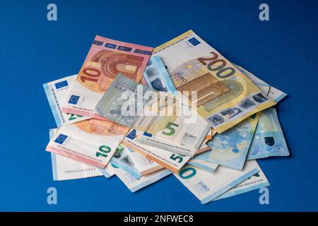 Auf dem Tisch liegt ein Stapel Banknoten in Stückelungen von fünf, zehn, zwanzig, fünfzig und zweihundert Euro. Gemischte Euro-Banknoten auf blauem Hintergrund. Stockfoto