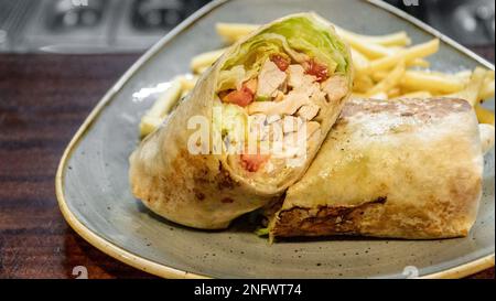 Ein leckeres Bild eines frisch zubereiteten Chicken Tortilla Wrap gefüllt mit Salat und serviert mit Pommes frites Stockfoto