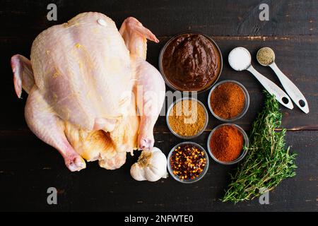 Apfelbutter geröstetes Hähnchen Zutaten auf einem Holztisch: Rohes Hähnchen, Apfelbutter und Gewürze auf dunklem Holzhintergrund Stockfoto