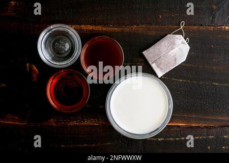 Rooibos Tea Latte Zutaten auf einem Holztisch: Rooibos Teebeutel, Milch und andere Zutaten auf dunklem Holzhintergrund Stockfoto