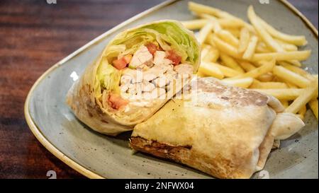 Ein leckeres Bild eines frisch zubereiteten Chicken Tortilla Wrap gefüllt mit Salat und serviert mit Pommes Frites aus nächster Nähe Stockfoto