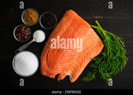 Frisches Lachsfilet, Meersalz und andere Inhaltsstoffe zur Herstellung von Lachs: Lachs, Salz, Kräuter und Gewürze, die zur Herstellung von haltbar gemachtem Lachs verwendet werden Stockfoto