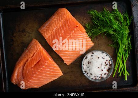 Lachsfilets, Dill und Salz gemischt mit Gewürzen auf einer Blechpfanne: Zutaten für die Herstellung von Lachs oder salzgepökeltem Lachs auf einem Backblech aus Metall Stockfoto
