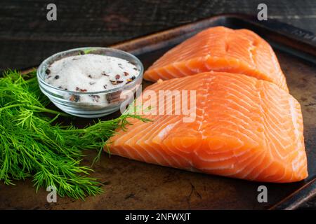 Lachsfilets, Dill und Salz gemischt mit Gewürzen auf einer Blechpfanne: Zutaten für die Herstellung von Lachs oder salzgepökeltem Lachs auf einem Backblech aus Metall Stockfoto