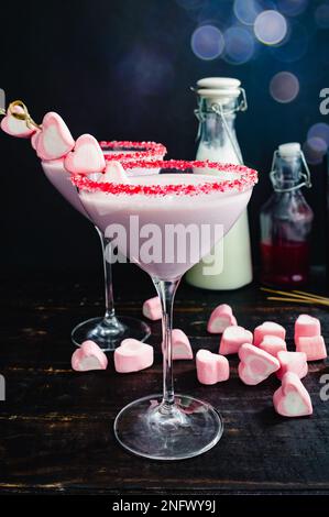 Valentinscocktail mit Himbeere und weißer Schokolade: Rosafarbener Cocktail in einem martini-Glas mit Streuseln und mit Herzmarshmallows garniert Stockfoto