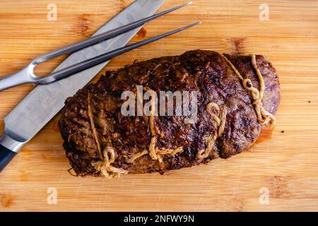 Gefülltes Flankensteak mit Prosciutto und Pilzen über dem Kopf: Unverschnittenes Steak Roulade auf einem Schneidebrett mit einem Schnitzmesser und einer Gabel Stockfoto