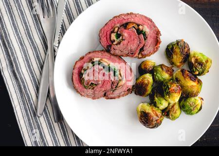 Gefülltes Flankensteak mit Prosciutto und Pilzen Abendessen: Scheiben Steak Roulade auf einem Teller mit gerösteten Rosenkohl Stockfoto