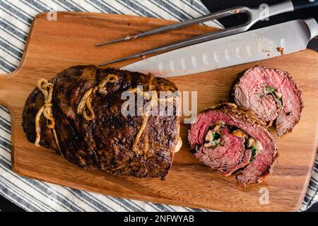 Geschnittenes gefülltes Flankensteak mit Prosciutto und Pilzen auf einem Schneidebrett: Scheiben von Steak-Roulade gefüllt mit Pilzen, Provolon und Rucola Stockfoto