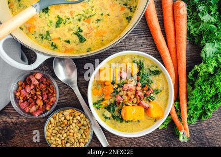 Süßkartoffelsuppe in einer Schüssel und holländischer Ofen mit Garnierungen: Cremige Gemüsesuppe garniert mit gebratenem Pancetta und gerösteten Pepitas Stockfoto