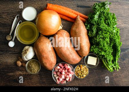 Süßkartoffelsuppe Zutaten auf einem Holztisch: Rohe Süßkartoffeln, Grünkohl, Pancetta und andere Suppenzutaten Stockfoto