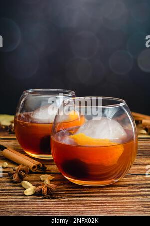 Gewürzter altmodischer Cocktail in einem Ballonglas mit Eiskugel: Bourbon Whiskey-Cocktail mit Orangenschale und Maraschino-Kirschgarnierung Stockfoto