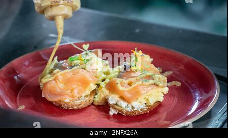 Ein frisch zubereiteter Räucherlachs und Rührei auf Toast, der aus nächster Nähe mit Honig und Senf bespritzt wird Stockfoto