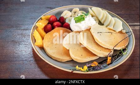 Ein Bild von frisch zubereiteten amerikanischen Pfannkuchen, abgetrennt mit frischem Obst und Sahne Stockfoto