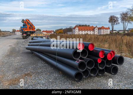 Auf der Baustelle liegen schwarze Kunststoffrohre mit roten Stopfen. Baufahrzeug im Hintergrund. Stockfoto