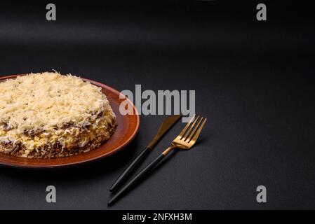 Köstlicher frischer Kuchen mit Hühnerleber, Eiern, Zwiebeln, Karotten und Mayonnaise auf einem Keramikteller auf dunklem Betonhintergrund Stockfoto