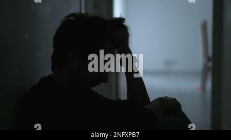 Ein depressiver junger Mann, der an einer psychischen Erkrankung leidet und sein Gesicht mit Bedauern verdeckt. Angstgefühle und Depressionen bei männlichen Personen Stockfoto