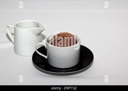 Schokoladenbomben in einem Becher mit heißer Milch, gefüllt mit Marshmallows und weißer Schokolade auf weißem Hintergrund Stockfoto