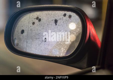 Der LEF-Seitenspiegel im Auto reflektiert nachts die Lichter der Stadt und Wassertropfen. Nahaufnahme eines hellen, unscharfen Hintergrunds. Stockfoto