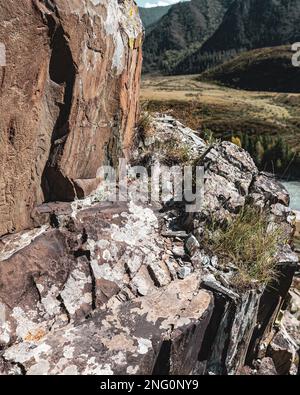 Felszeichnungen von alten Menschen und Rehe auf den Steinen hinter dem Panorama der Berge und des Altai-Flusses während des Tages. Stockfoto