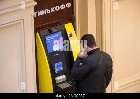 Moskau, Russland. 17. Februar 2023. Ein Mann hebt Geld von einem Geldautomaten der Tinkoff Bank auf dem Territorium eines KAUGUMMILADENS im Zentrum von Moskau, Russland ab Stockfoto