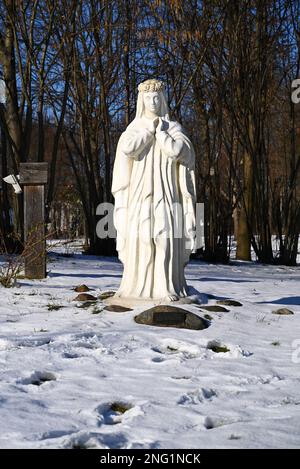 Lublin, Polen. 08. Februar 2023 Weiße Jungfrau Maria im Schnee vor der alten Kirche im Winter. Stockfoto