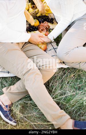 Mann und Frau sitzen auf einer Decke und halten Händchen. Gekürzt Stockfoto