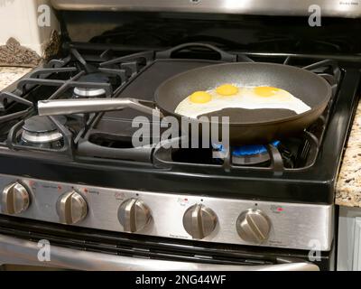 Eier, die in Pfannkuchen oder Bratpfannen braten, um sie in einem Haus in den USA auf einem Gasherd oder Herd zu kochen. Stockfoto