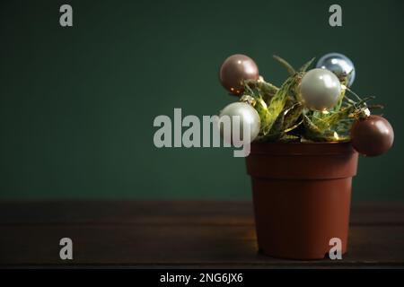 Schöner Kaktus mit Weihnachtsbällen und festlichen Lichtern auf einem Holztisch vor grünem Hintergrund, Platz für Text Stockfoto