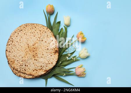 Leckere Matzen und frische Blumen auf hellblauem Hintergrund, flach liegend. Pessach-Feier Stockfoto