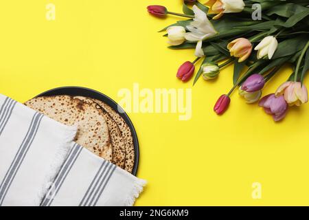 Leckere Matzen und frische Blumen auf gelbem Hintergrund, flach liegend. Pessach-Feier Stockfoto