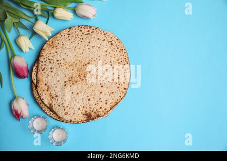 Schmackhafte Matzen, Tulpen und Kerzen auf hellblauem Hintergrund, flach liegend mit Platz für Text. Pessach-Feier Stockfoto