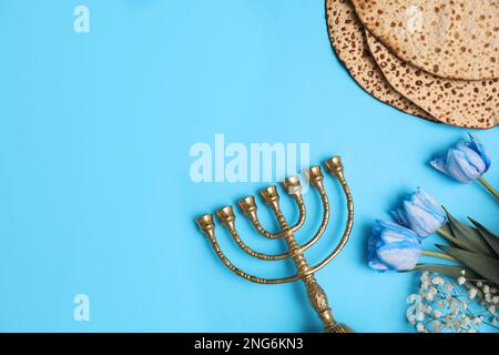 Schmackhafte Matzen, Blumen und Menora auf hellblauem Hintergrund, flach liegend mit Platz für Text. Pessach-Feier Stockfoto