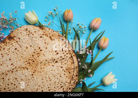 Leckere Matzen und frische Blumen auf hellblauem Hintergrund, flach liegend. Pessach-Feier Stockfoto