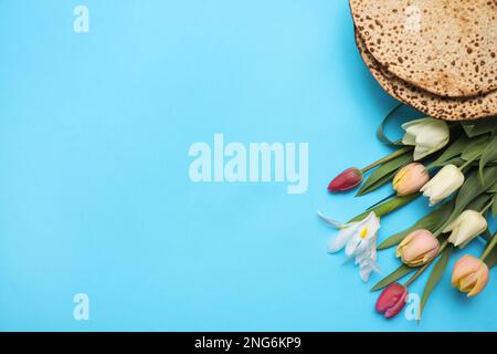 Schmackhafte Matzen und frische Tulpen auf hellblauem Hintergrund, flach liegend mit Platz für Text. Pessach-Feier Stockfoto