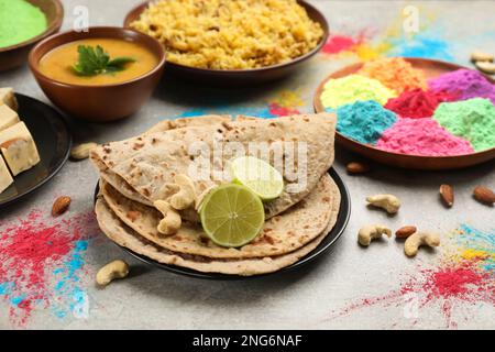 Traditionelles indisches Essen und Farbpulver auf grauem Tisch. Holi-Festival-Feier Stockfoto