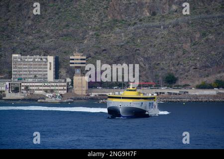 Gelbe Hochgeschwindigkeitsfähre verlässt den Hafen in Santa Cruz, Teneriffa auf den Kanarischen Inseln. Hafengebäude im Hintergrund. Stockfoto