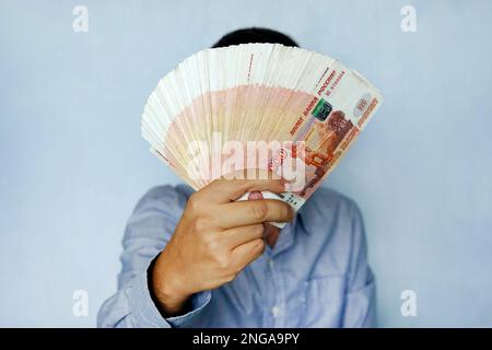 Stapel von Banknoten 5 000 russische Rubel in der Hand des Menschen auf blauem Hintergrund. Bündel Banknoten von 5000 Rubel der Russischen Föderation. Stockfoto