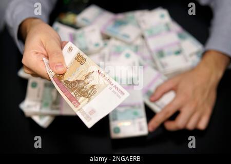 Der Mann hält einen Hundert-Dollar-Schein in russischen Rubeln und hält die Hände von Millionen Rubel. Das Konzept von Gier, Wucher oder Nächstenliebe. Stockfoto