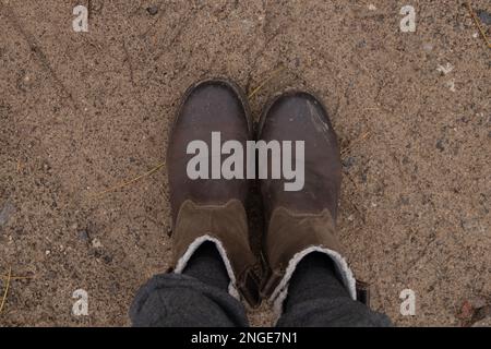 Weibliche Beine in grauen Hosen und braune Stiefel auf dem Boden im Wald am Herbstnachmittag für einen Spaziergang Stockfoto