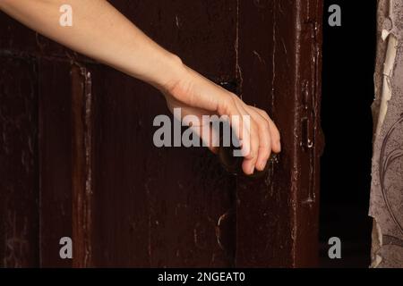 Die Hand einer Frau öffnet die alte dunkle Tür zum Schlafzimmer Stockfoto